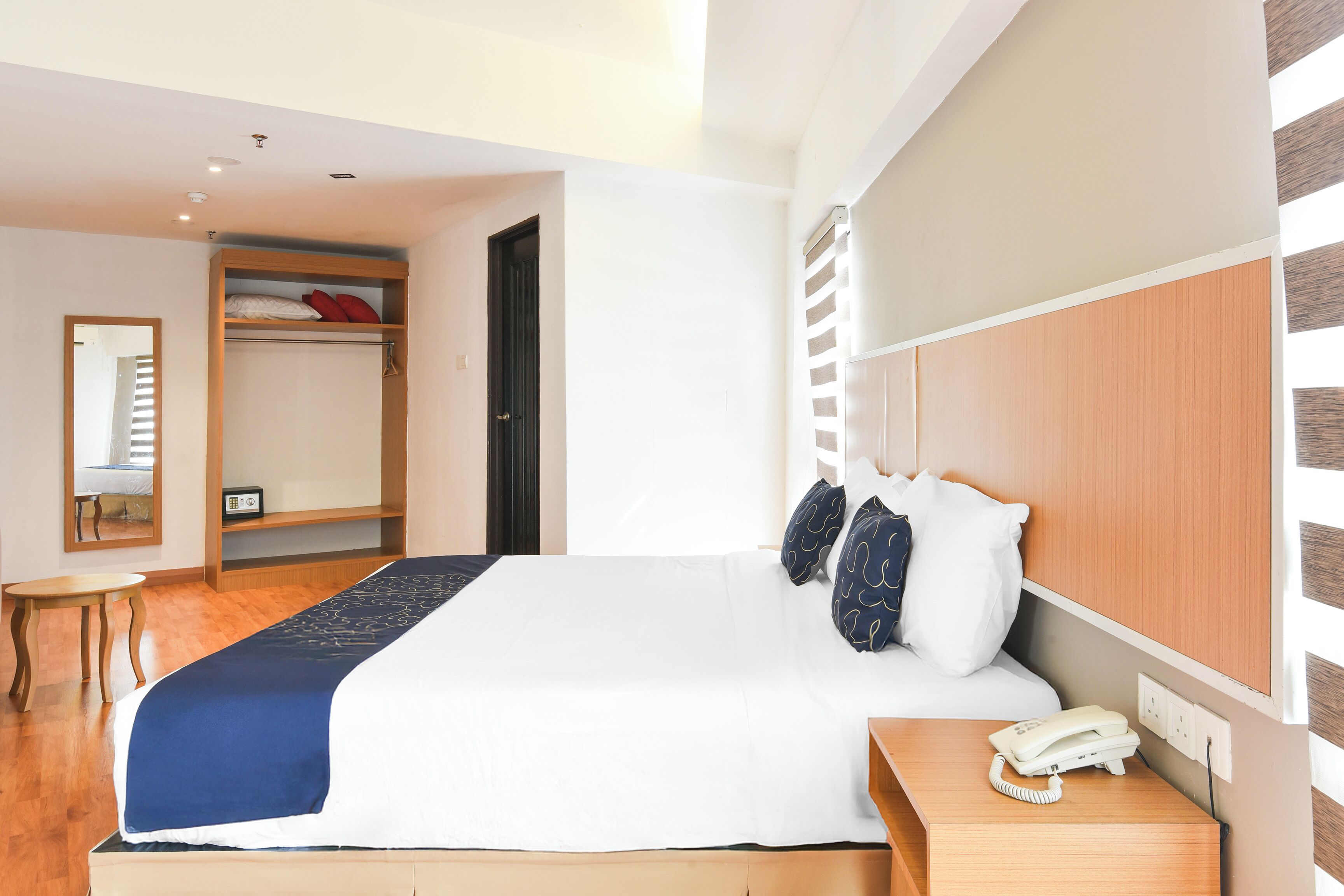 Une chambre d’hôtel avec un grand lit, une table de chevet avec un téléphone, une armoire et une petite table.