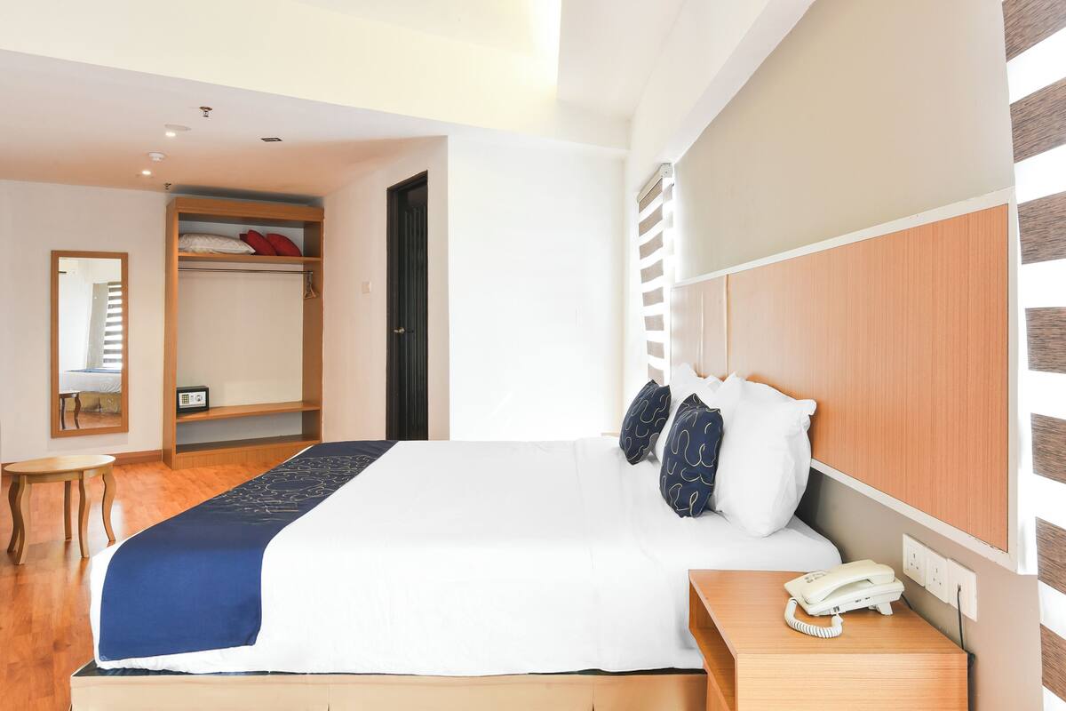 Een hotelkamer met een groot bed, een nachtkastje met een telefoon, een kledingkast en een klein tafeltje.
