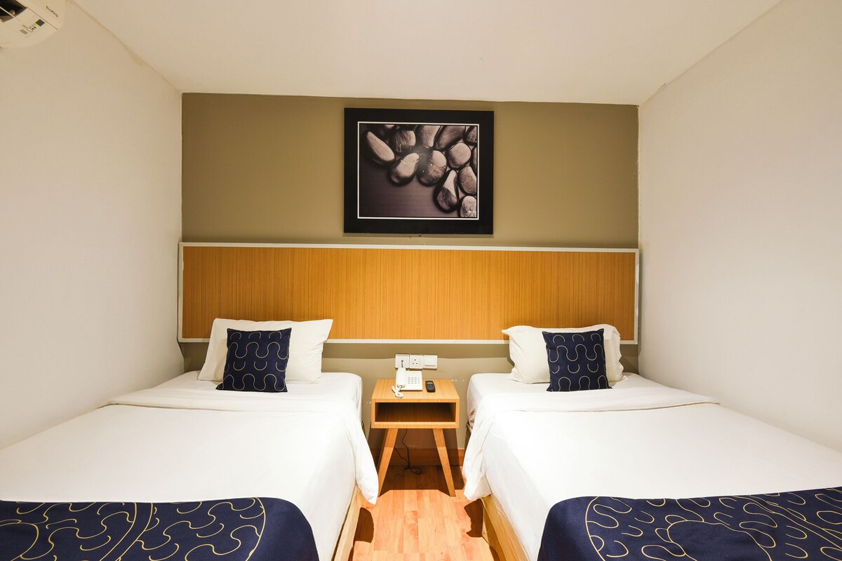 Ein Hotelzimmer mit zwei Betten, einem Nachttisch aus Holz mit Telefon und Fernbedienung sowie einem gerahmten Bild an der Wand.