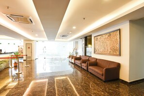 Un vestíbulo moderno con piso de mármol, una mesa de recepción, una zona de estar con sofás y un cuadro abstracto grande en la pared.
