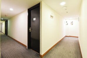 Pasillo de hotel con pisos alfombrados, una puerta negra con un letrero de número y un interruptor de luz en la pared.