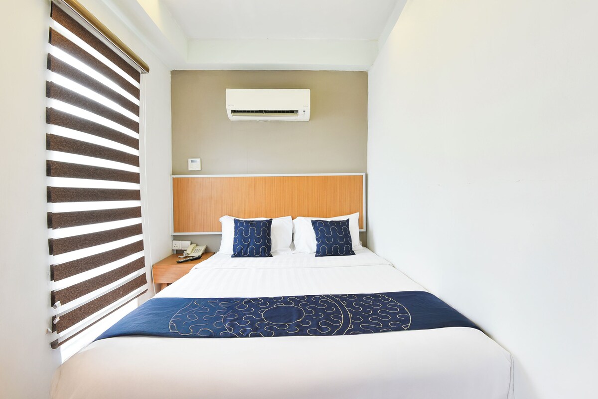 A neatly made bed with a blue patterned bedspread, a wooden headboard, and a white air conditioning unit above it.