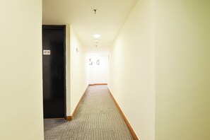 Ein schmaler Flur mit Teppichboden, einer schwarzen Tür links und einer weißen Tür am Ende.