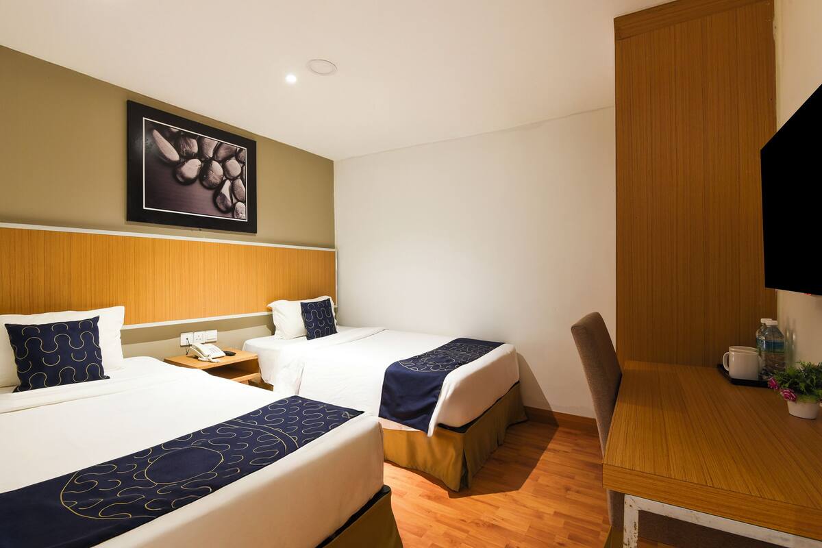 Een hotelkamer met twee bedden, een houten bureau, een stoel, een telefoon en een lijst met een foto aan de muur.