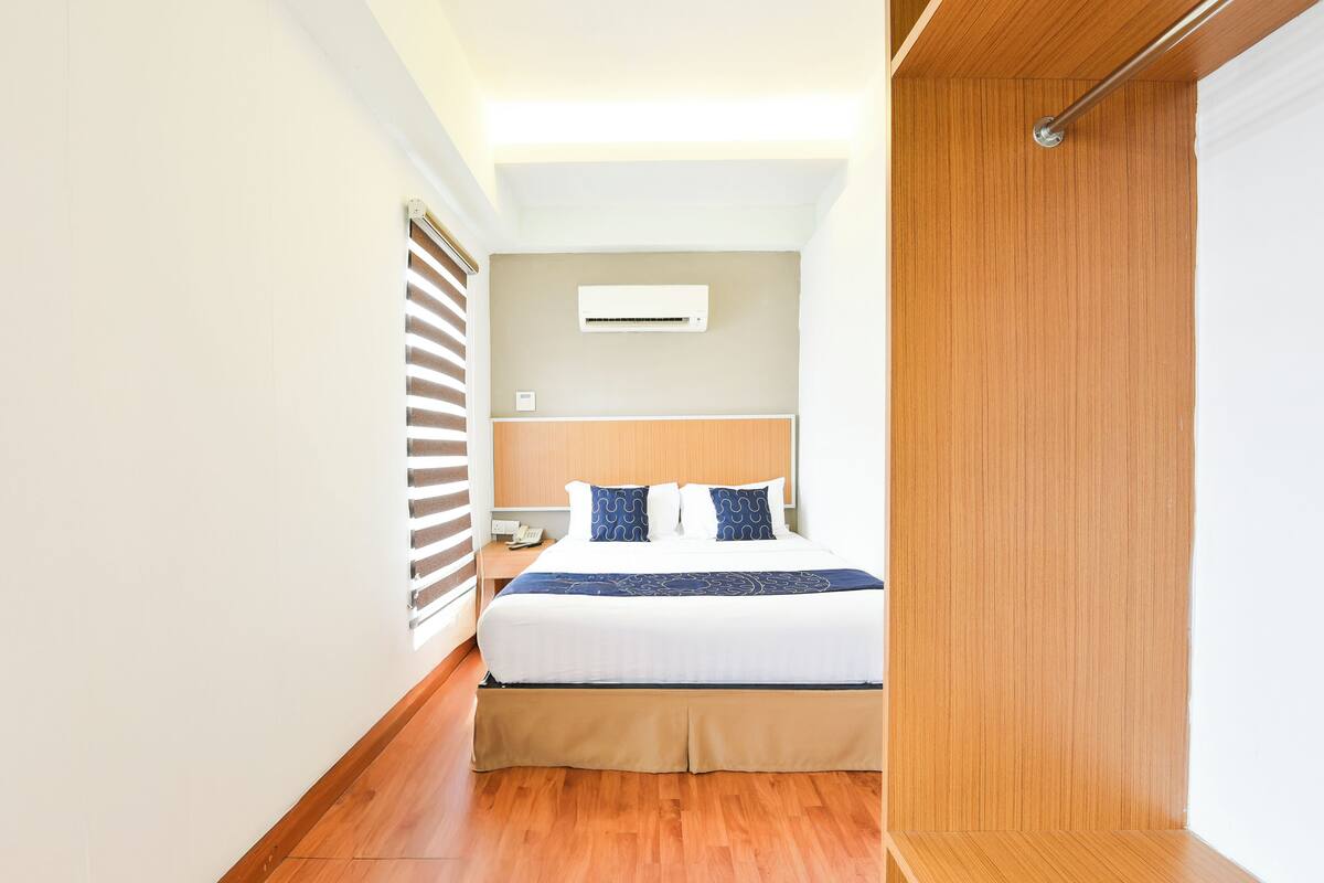 Een hotelkamer met een bed, een houten vloer, een witte muur en een plafondlamp.