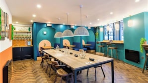 A modern restaurant with a long wooden table, blue walls, and pendant lights. - Clifton Village - Your Apartment (Bristol)
