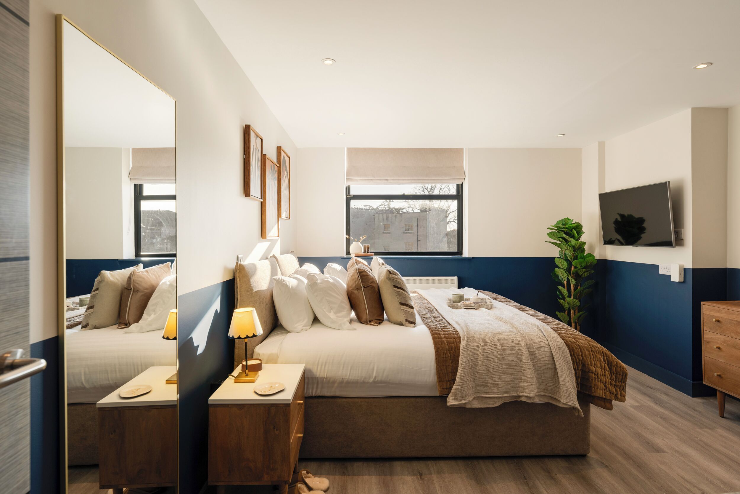 Une chambre à coucher moderne avec un lit, une table de chevet, une lampe et un grand miroir.