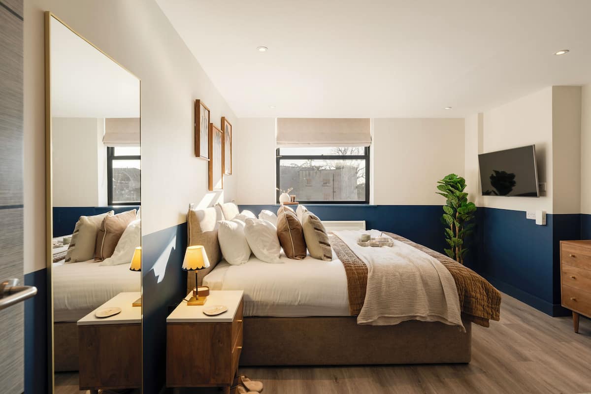 Un dormitorio moderno con cama, mesita de noche, lámpara y un espejo grande.