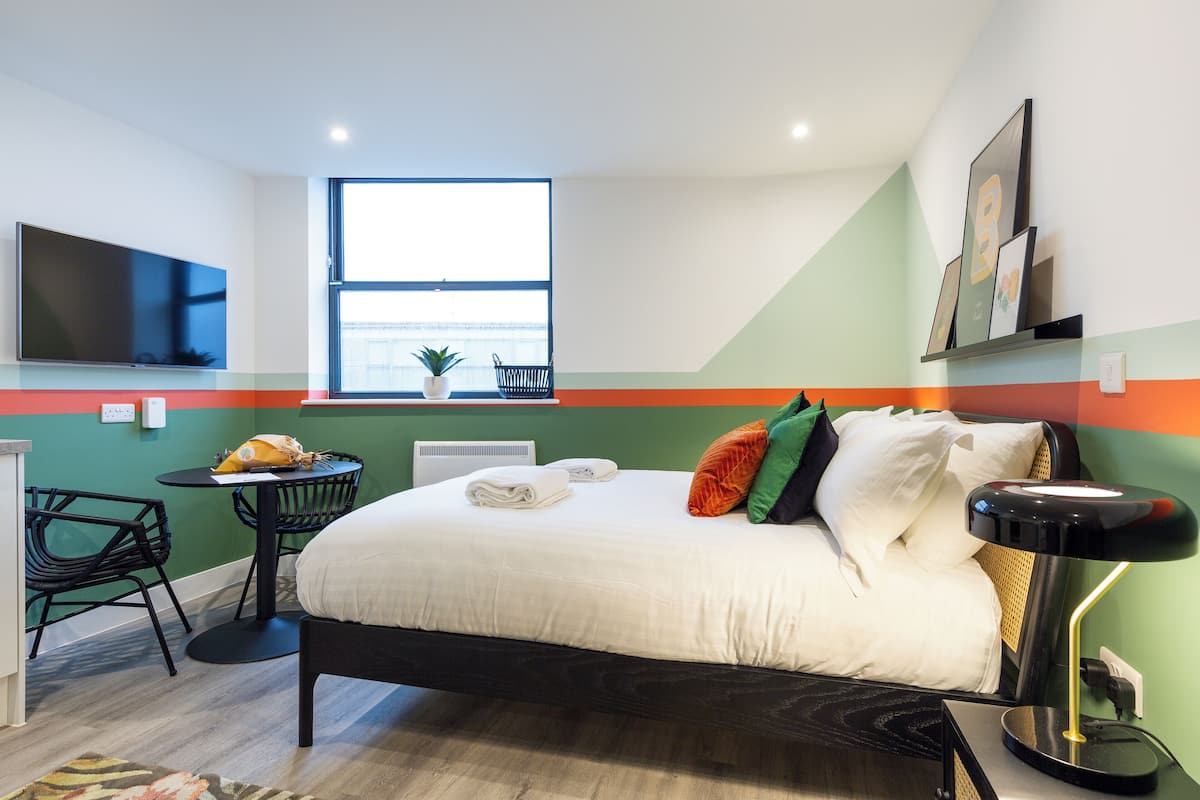 Una habitación de hotel moderna con una cama, un escritorio, una silla, un televisor y una ventana con vistas.