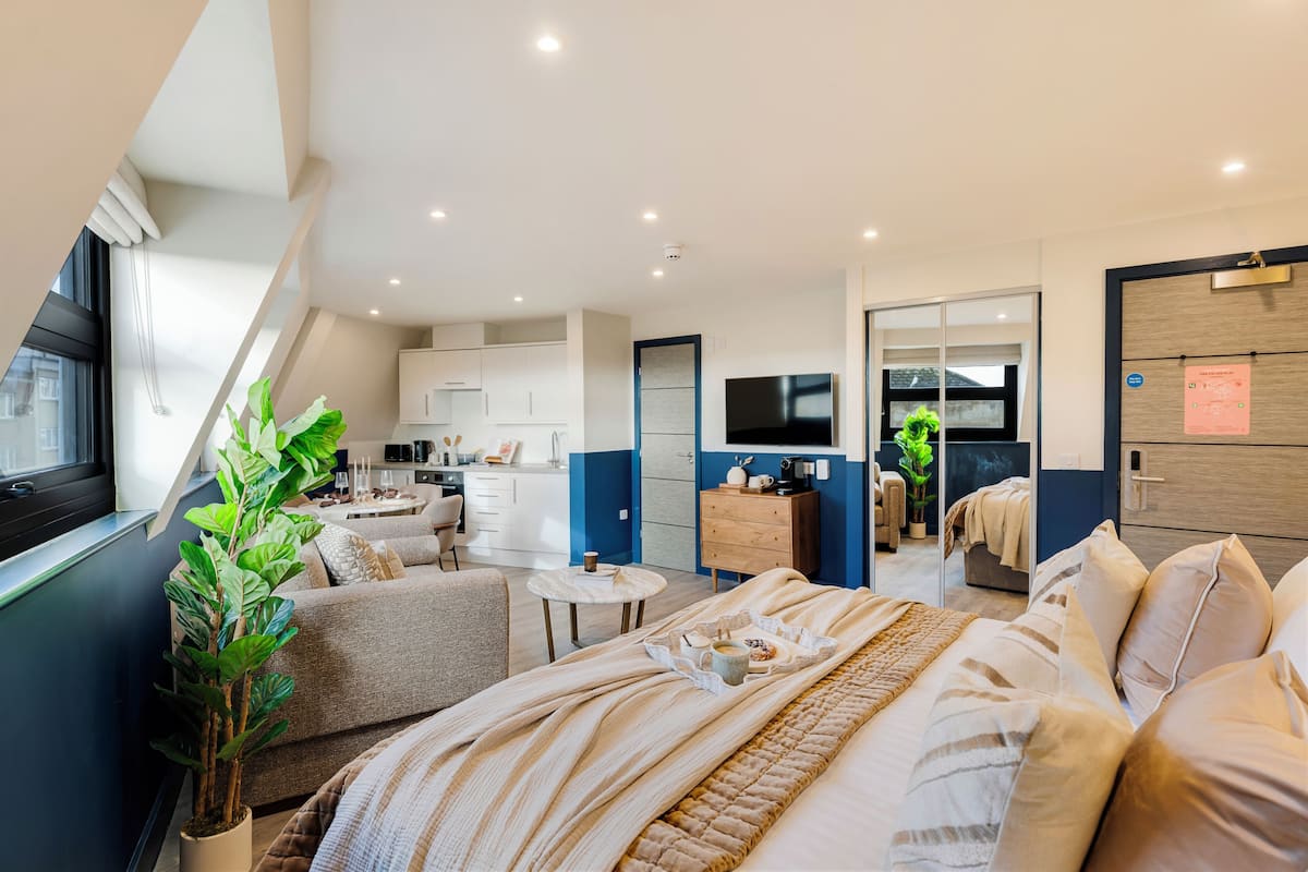 Una habitación de hotel moderna con una cama grande, un pequeño rincón de descanso, una kitchenette y un baño.