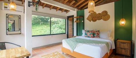 Een slaapkamer met een bed, een tafel, een stoel, een plafondventilator en een raam met uitzicht op groen.