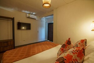 Un dormitorio con una cama, un televisor en la pared y una puerta que da a otra habitación.