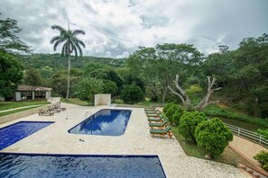 A swimming pool with lounge chairs, surrounded by greenery and a hill in the background. - Tres Lagos Hotel (San Jerónimo)