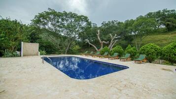 A swimming pool with a stone deck, surrounded by green lounge chairs and trees.