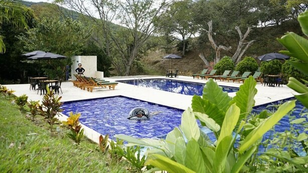A swimming pool with lounge chairs and umbrellas, surrounded by greenery and trees. - Tres Lagos Hotel (San Jerónimo)