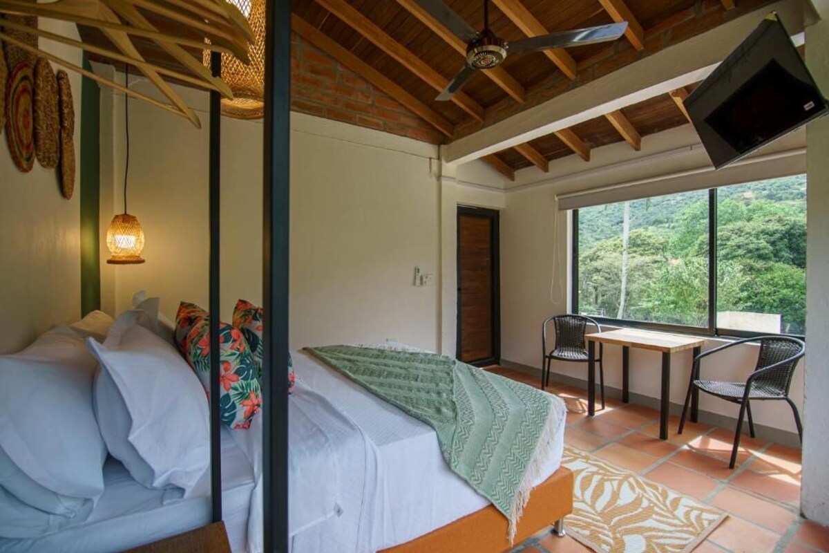 A bedroom with a bed, a table, chairs, a TV, and a view of the outdoors.