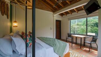 A bedroom with a bed, a table, chairs, a TV, and a view of the outdoors.