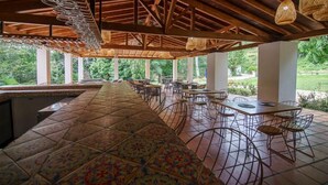 A covered outdoor dining area with tiled flooring, metal chairs, and hanging light fixtures. - Tres Lagos Hotel (San Jerónimo)