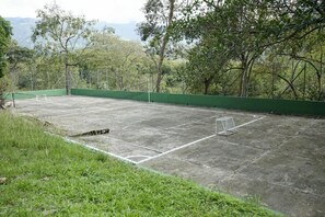 An outdoor sports court with a green fence, surrounded by trees and grass. - Tres Lagos Hotel (San Jerónimo)