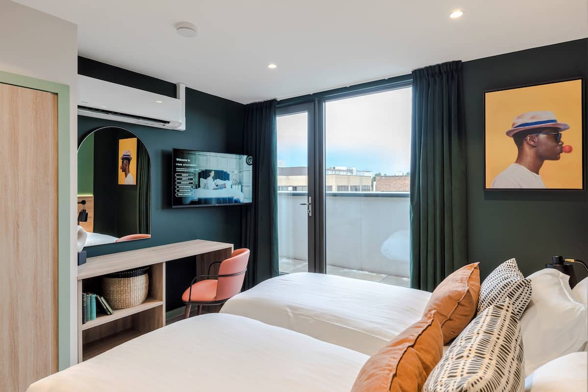 Une chambre d’hôtel moderne, dotée d’un grand lit, d’un bureau, d’une chaise et offrant une vue sur la ville par la fenêtre.