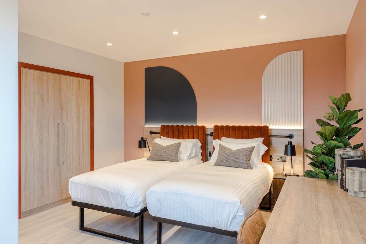 Une chambre moderne avec deux lits, une armoire en bois, un grand miroir et une plante en pot.