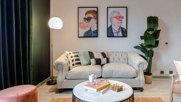 A living room with a sofa, a coffee table, a lamp, a plant, and two framed pictures on the wall.
