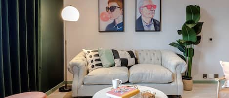 Ein Wohnzimmer mit einer Couch, einem Couchtisch, einer Lampe, einer Pflanze und zwei gerahmten Bildern an der Wand.