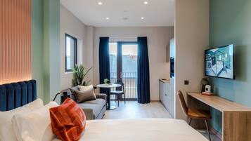 A modern hotel room with a bed, a sofa, a desk, a chair, a small table, and a TV.
