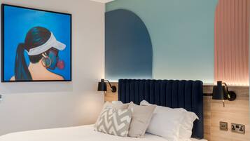 A modern hotel room with a large bed, a headboard with built-in lighting, a wall-mounted artwork, and a bedside table.