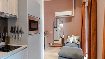 Una cocina moderna con microondas, estufa y cuchillos en la pared, un sofá con cojines y un equipo de aire acondicionado.