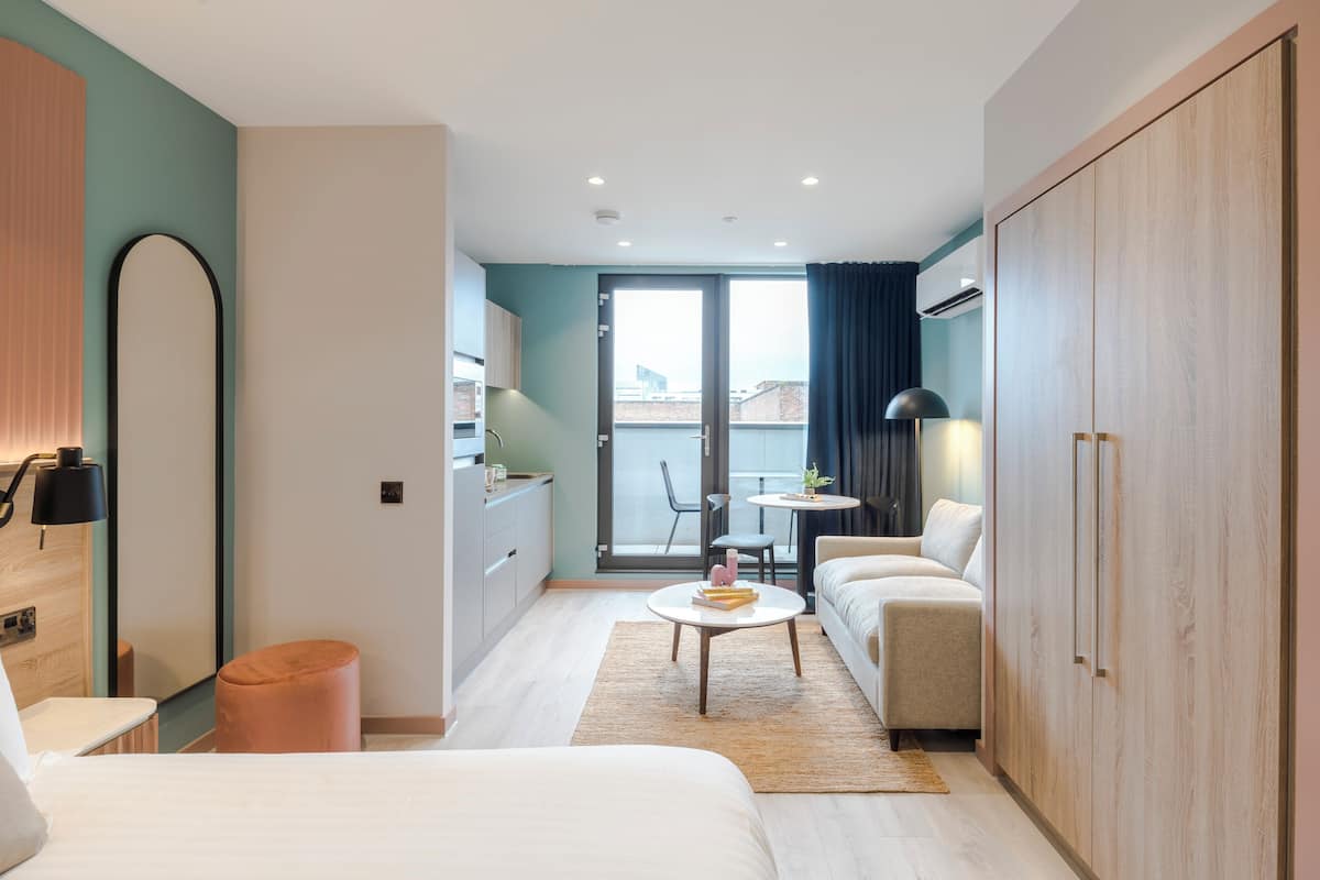 Une chambre d’hôtel moderne équipée d’un lit, d’un canapé, d’une petite table et d’une armoire. Elle dispose également d’un balcon avec vue sur la ville.