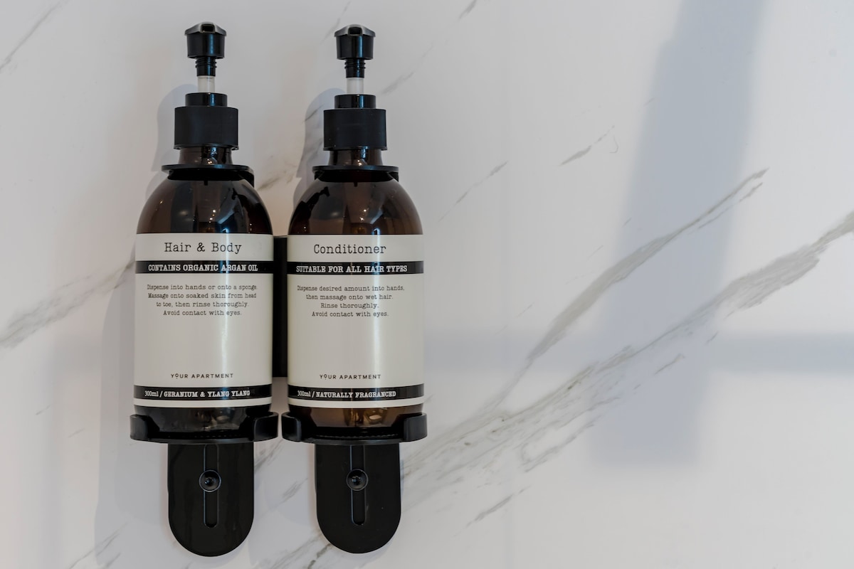Deux flacons d’après-shampoing et de soin pour le corps, posés sur une surface en marbre.