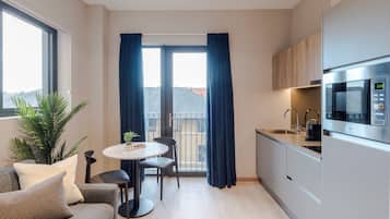A compact kitchen with a dining area, a sofa, and a large window with curtains.