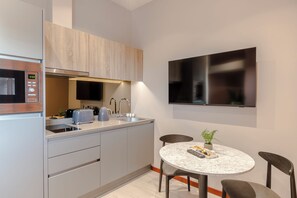 A modern kitchen with a built-in microwave, toaster, and sink. There is a round table with chairs and a small potted plant on the counter. - Milton Keynes - Your Apartment (Milton Keynes)