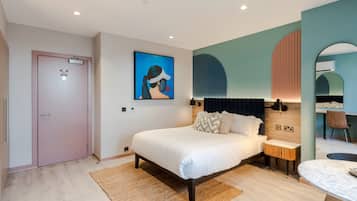 A modern bedroom with a large bed, bedside tables, a small seating area, and a dining table.