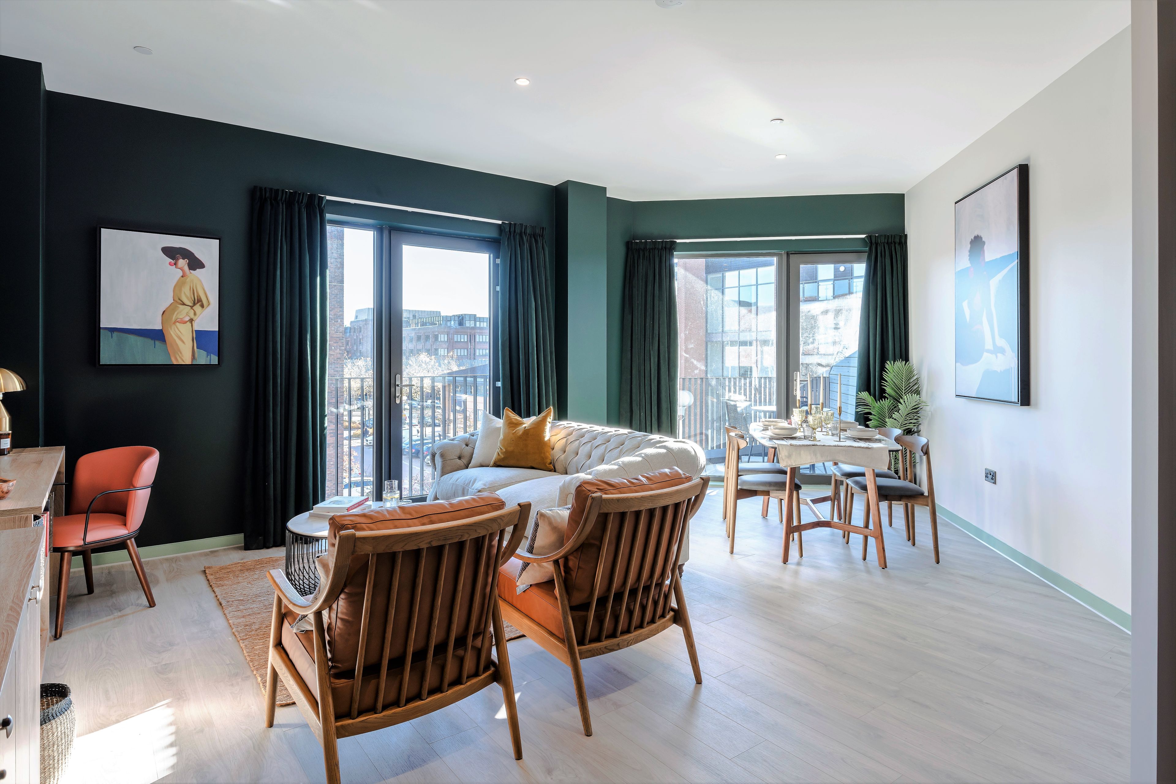 A modern living room with a sofa, wooden chairs, a dining table, and large windows offering a city view.