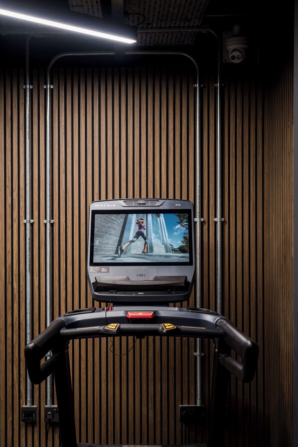 Una cinta de correr con pantalla digital, frente a una pared de madera con listones verticales.