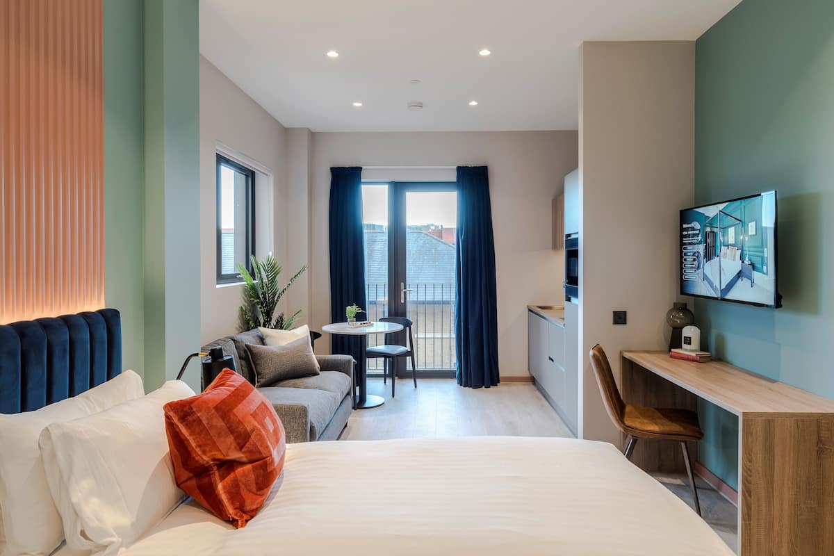 Une chambre d’hôtel moderne équipée d’un lit, d’un canapé, d’un bureau, d’une chaise, d’une petite table et d’un téléviseur.