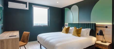 A modern bedroom with a large bed, a desk, and a chair.