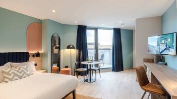 A modern hotel room with a bed, a desk, a chair, a round table, and a balcony with curtains.