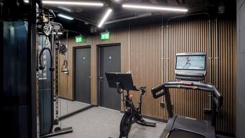 A gym with exercise equipment, a treadmill, and a wall-mounted TV screen.