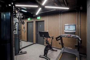 A gym with exercise equipment, a treadmill, and a wall-mounted TV screen.