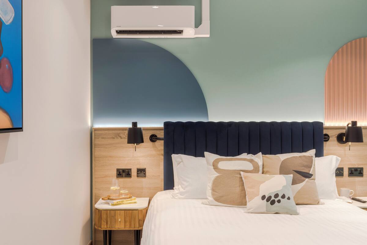 Une chambre d’hôtel équipée d’un lit, d’une table de chevet, d’une lampe et d’un climatiseur fixé au mur.