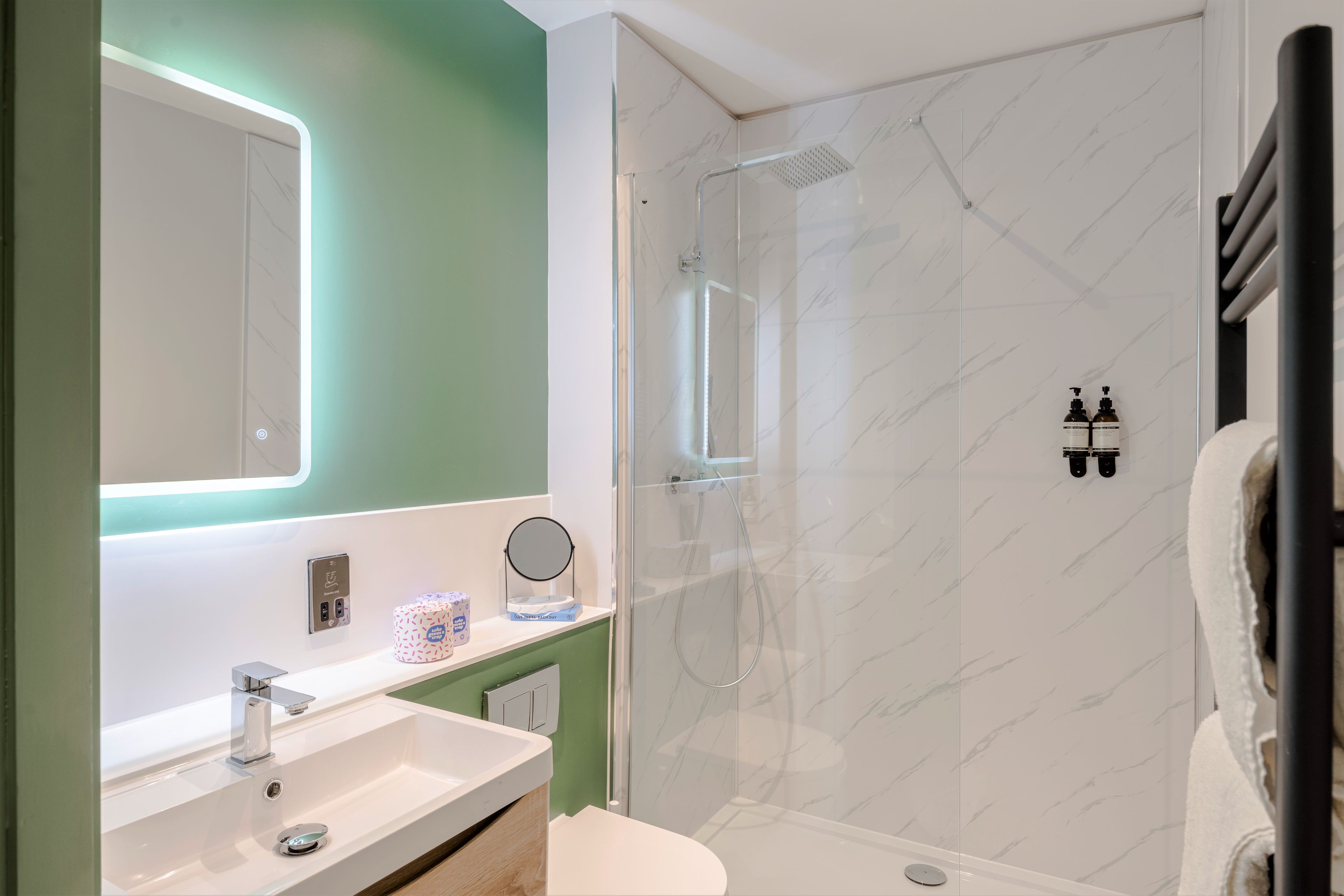 A modern bathroom with a glass-enclosed shower, a sink with a mirror, and toiletries on the counter.