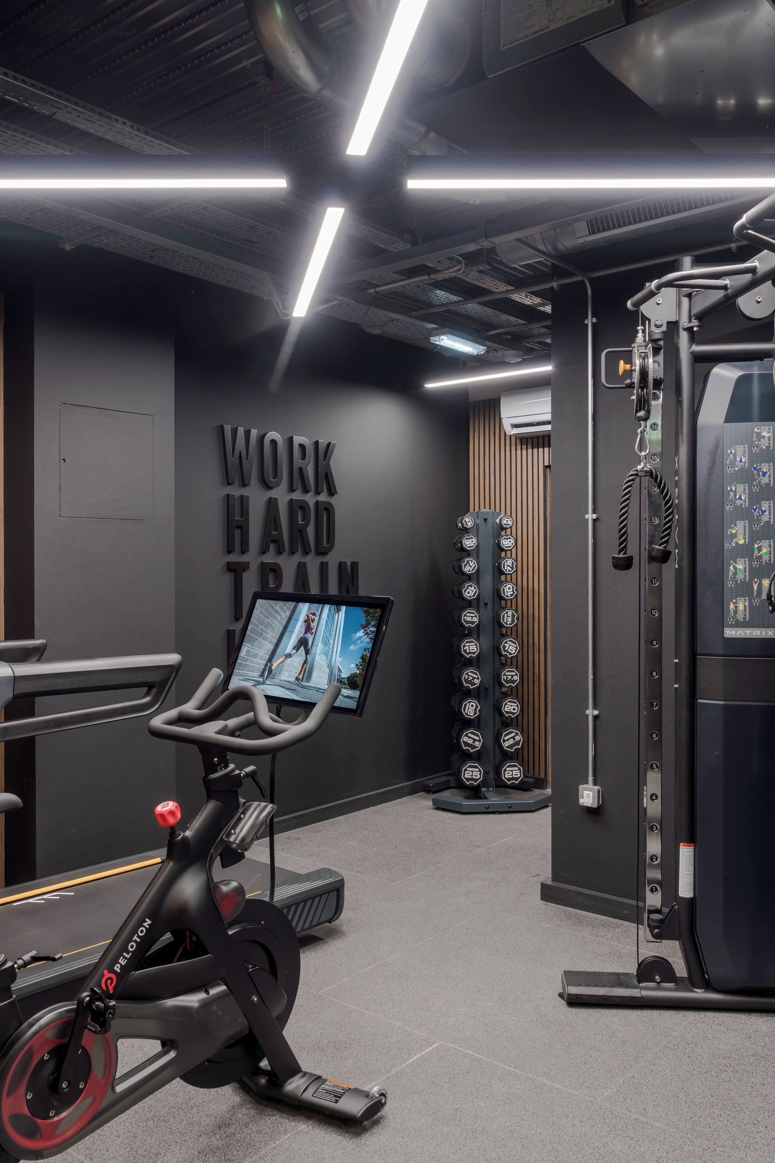 A gym with exercise equipment, a wall with motivational text, and a digital screen displaying an image.