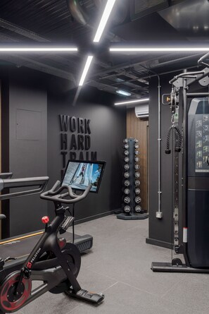 Un gimnasio con equipo de ejercicio, una pared con texto motivacional y una pantalla digital mostrando una imagen.