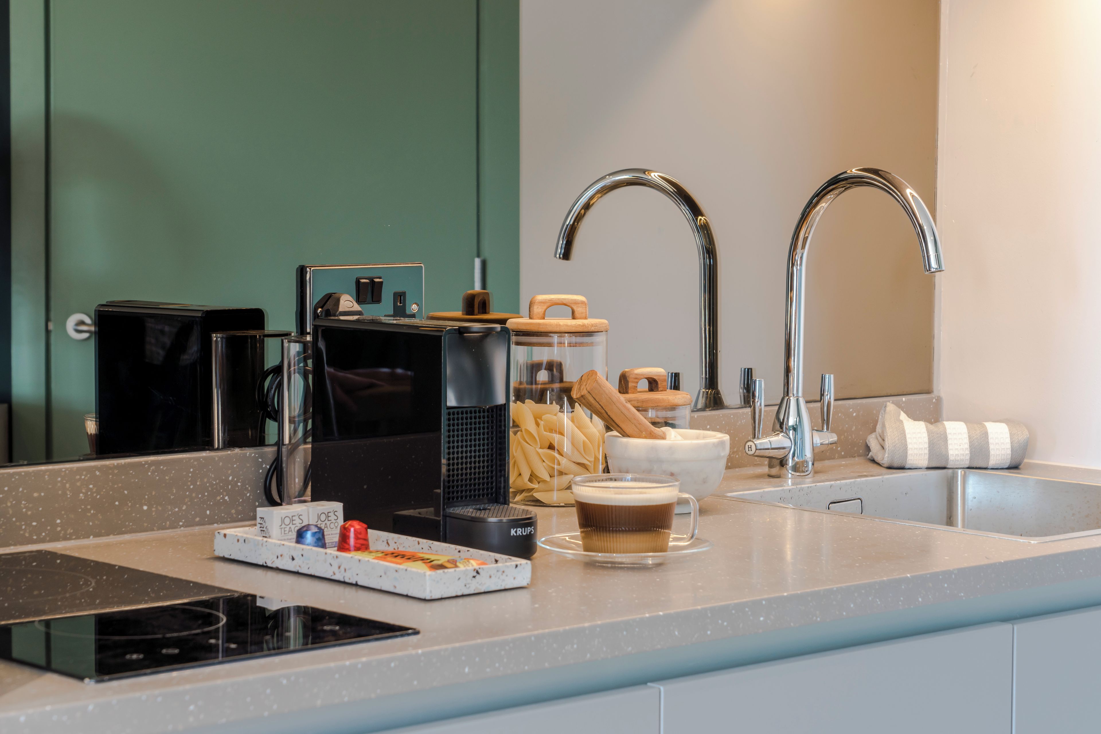 A modern kitchen with a built-in coffee machine, a kettle, and a coffee cup on the counter.