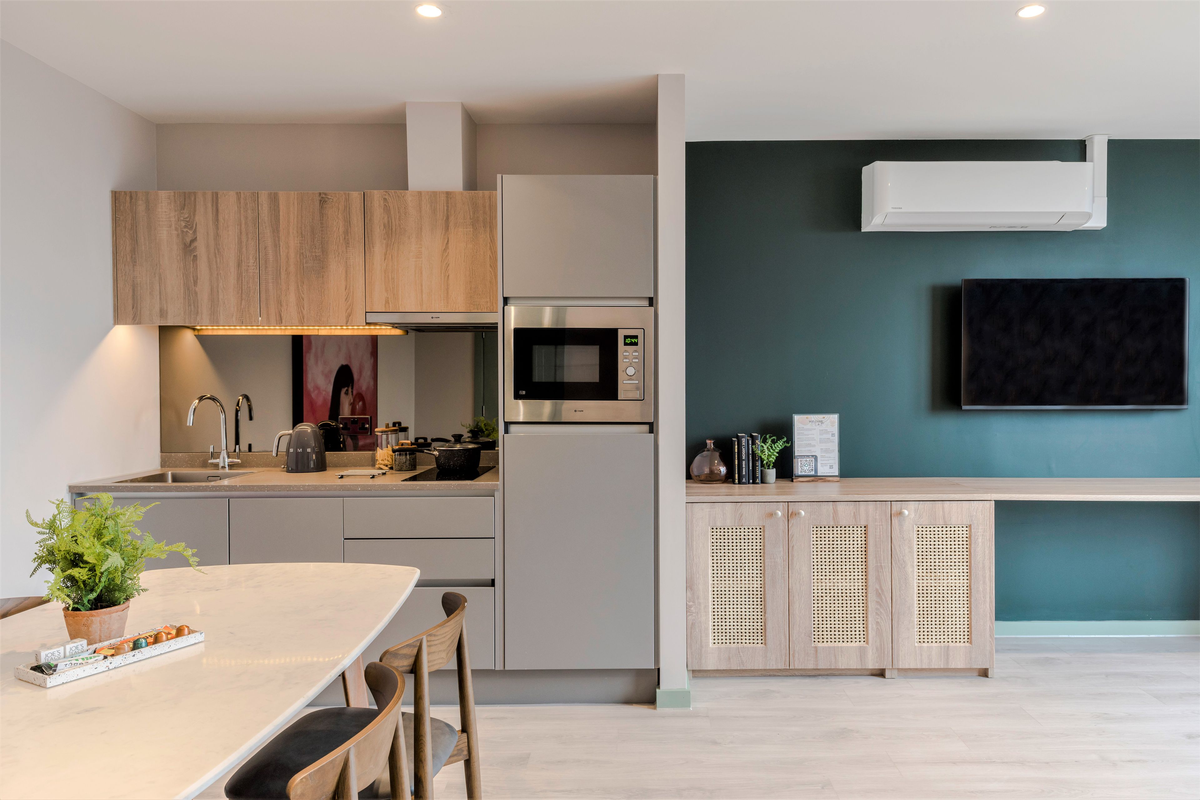Cocina moderna con microondas, estufa y pileta integrados. Hay un comedor con mesa y sillas, y un televisor montado en la pared.