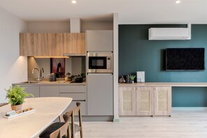 Cocina moderna con microondas, estufa y pileta integrados. Hay un comedor con mesa y sillas, y un televisor montado en la pared.