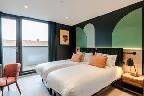 A modern hotel room with two beds, a chair, a nightstand, and a large window offering a city view. - Milton Keynes - Your Apartment (Milton Keynes)